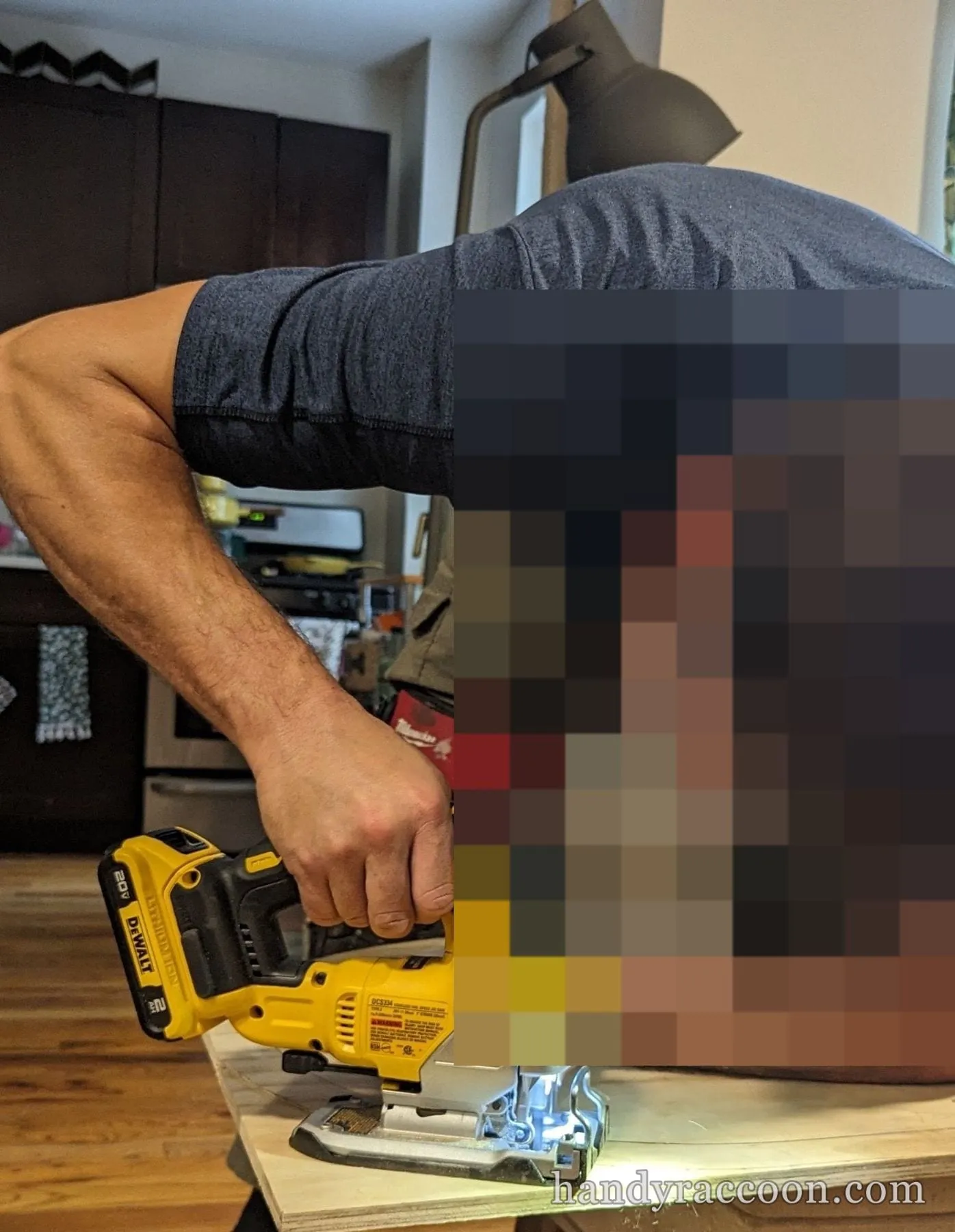 A person in safety glasses leans over a plywood sheet cutting a curve with a cordless jigsaw.