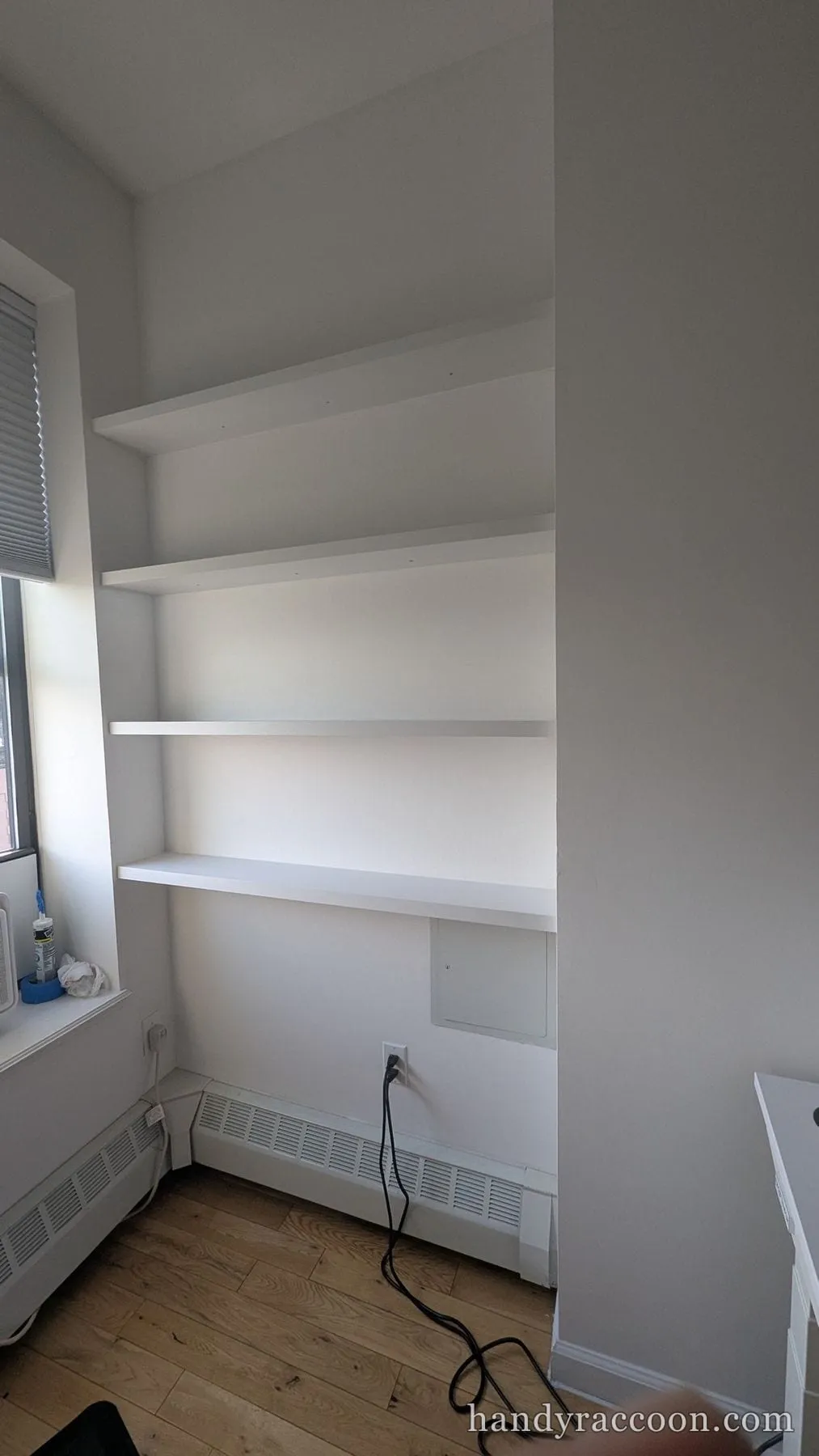 Long white floating shelves mounted across a bright alcove beside a window.