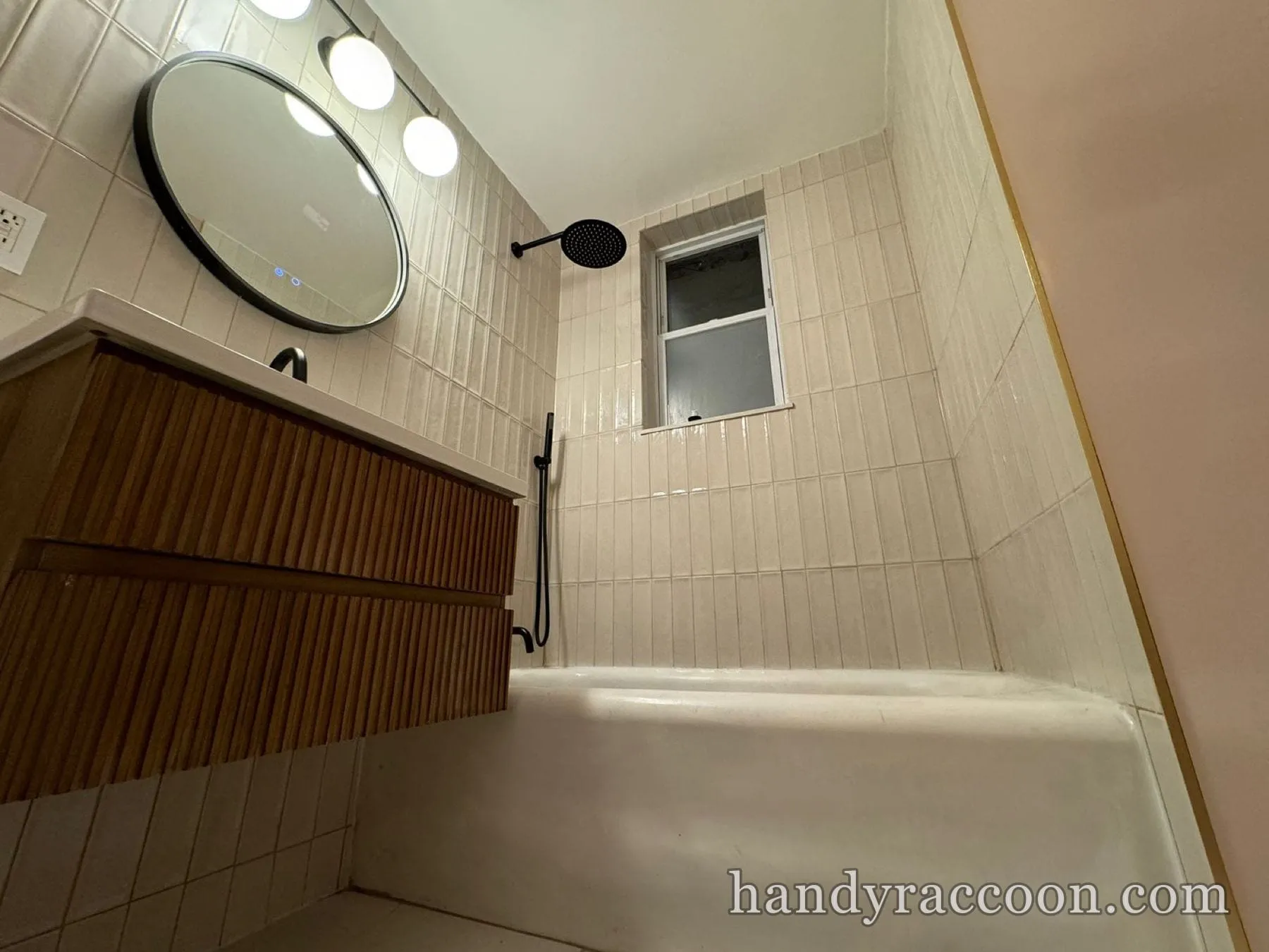 Renovated bathroom with vertical cream tile, wood floating vanity, round mirror and black rain shower.