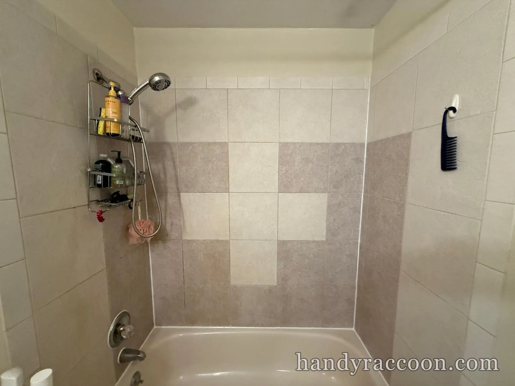 Beige tile tub surround with a cross-pattern accent, wire caddy and chrome shower head.