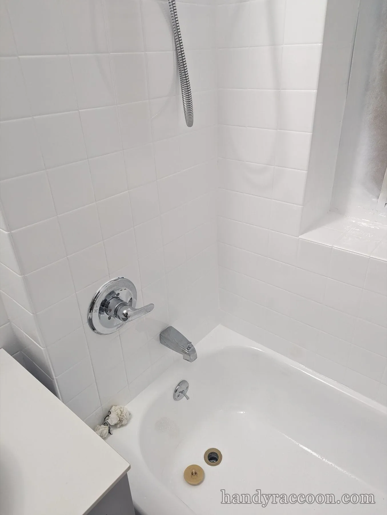 White square-tile tub surround with a chrome lever valve and freshly caulked corners.