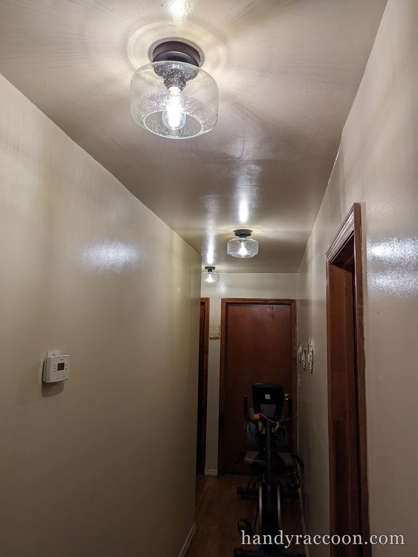 Two clear glass schoolhouse-style flush ceiling lights lit down a narrow hallway.