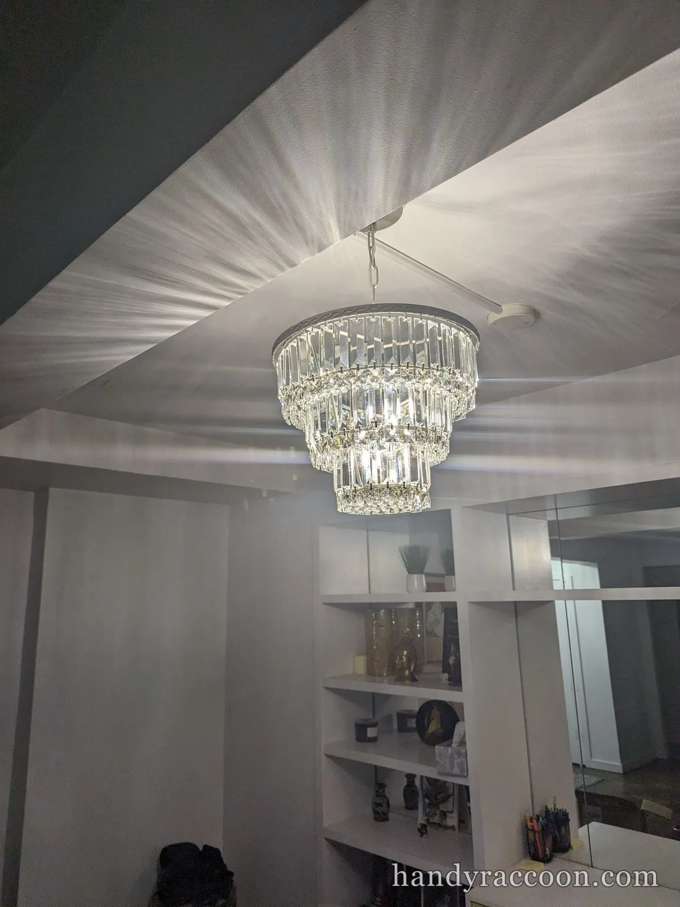 Multi-tier crystal chandelier lit and hanging above white cube shelving.