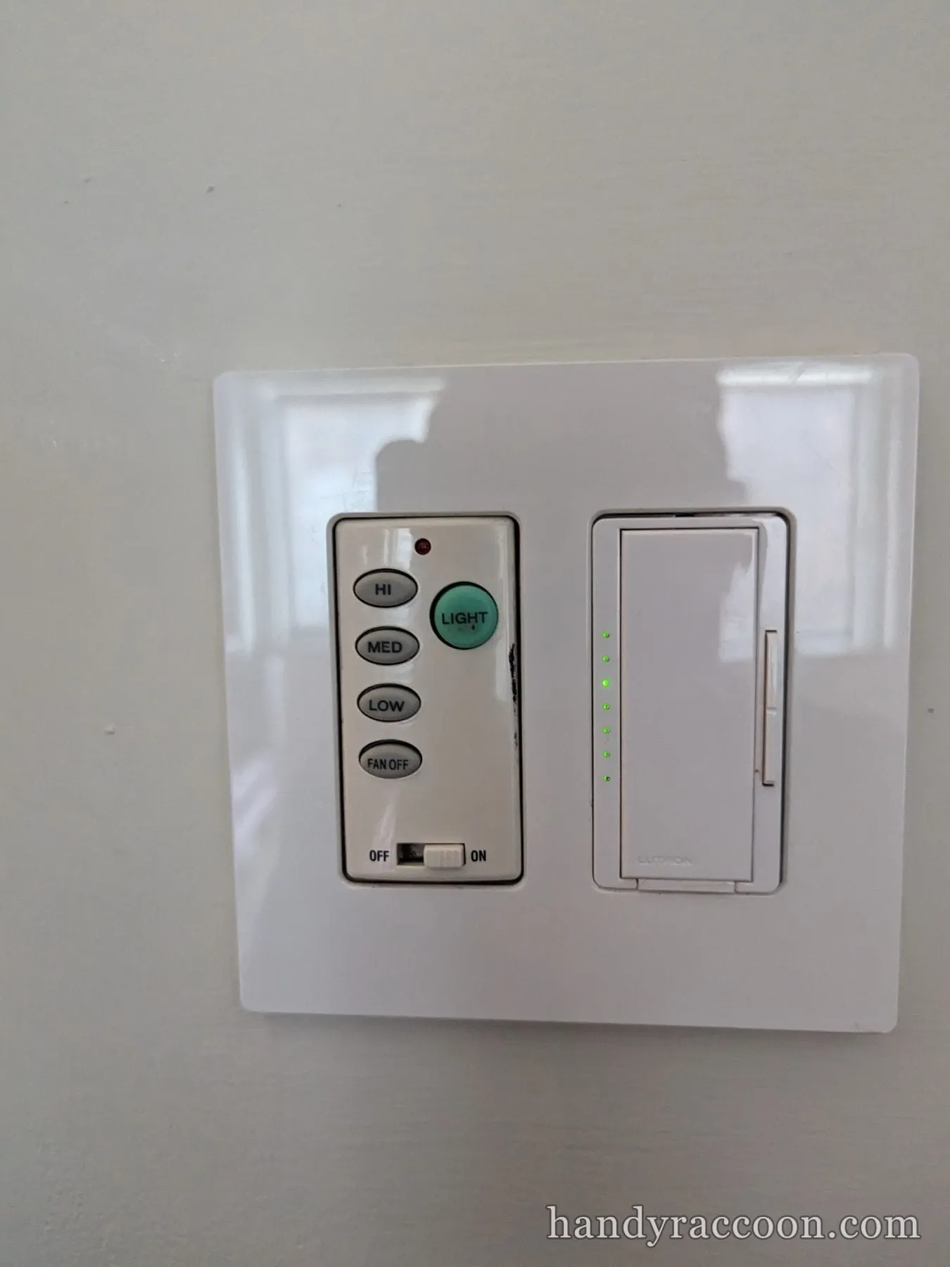 Wall plate with a fan speed remote control beside a lit dimmer slider.