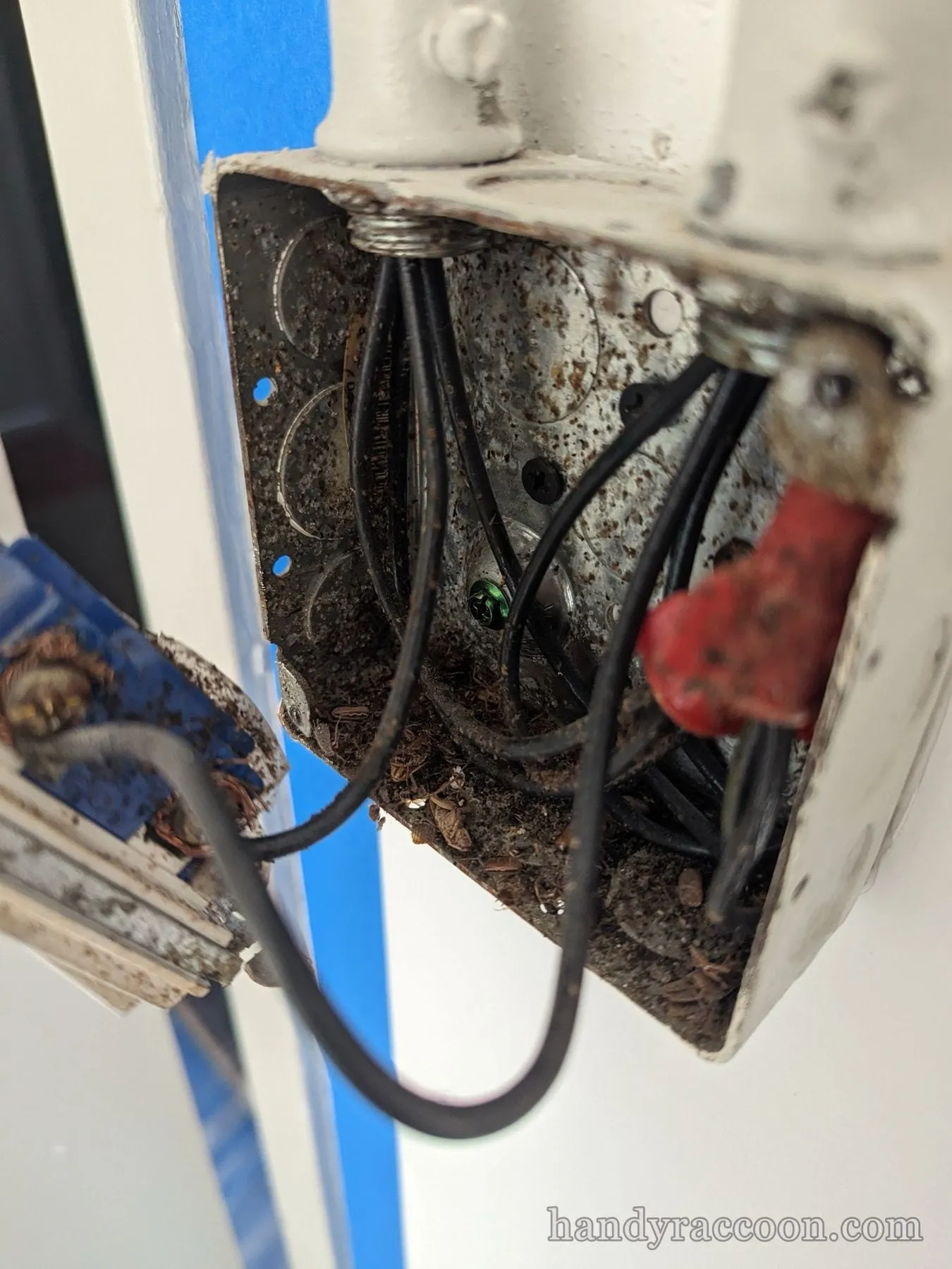 Corroded metal junction box with black wires, a red wire nut and a green ground screw.