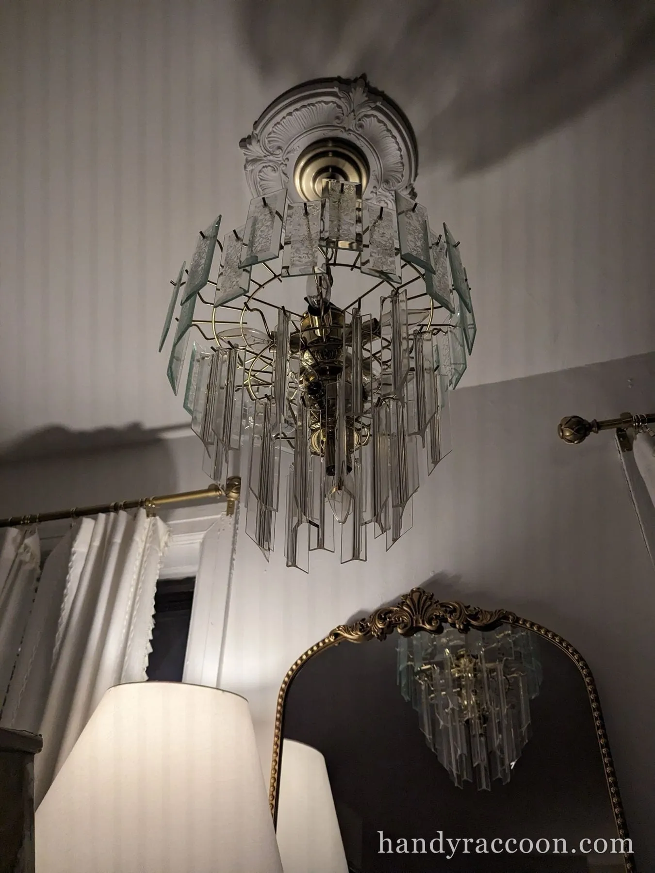 Tiered clear-glass chandelier mounted on a decorative white ceiling medallion, reflected in a mirror.