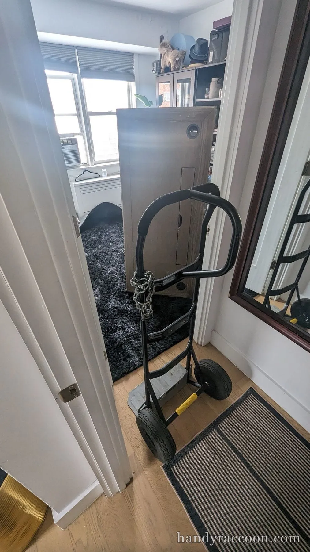 A large grey cabinet secured with a chain to a black hand truck in an apartment doorway.