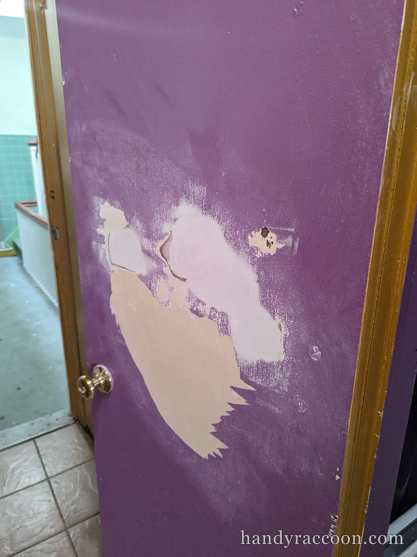 Close up of sanded filler patches on a purple door beside a brass knob.