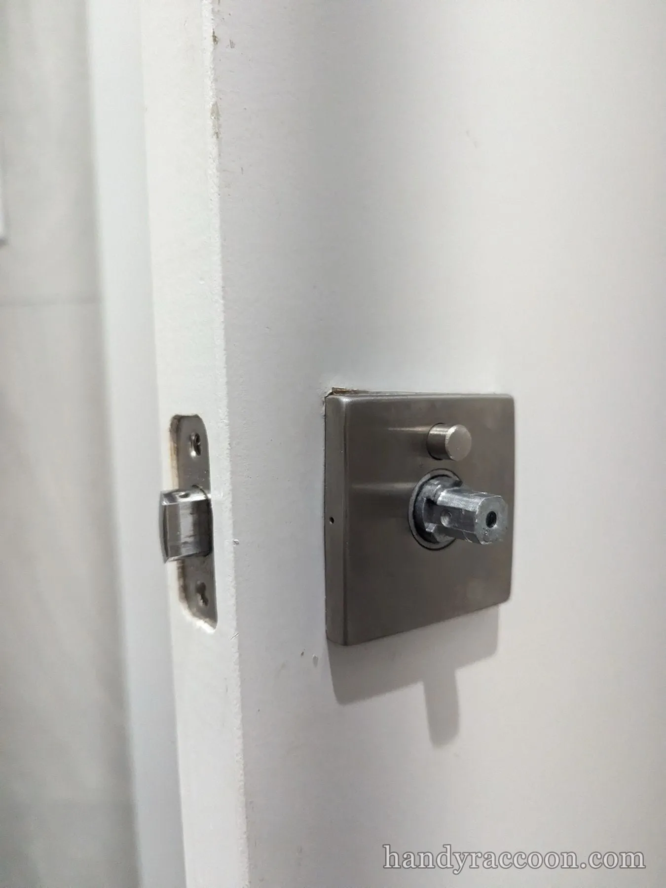 Close-up of a square stainless deadbolt thumbturn on a white door with the latch bolt on the jamb.
