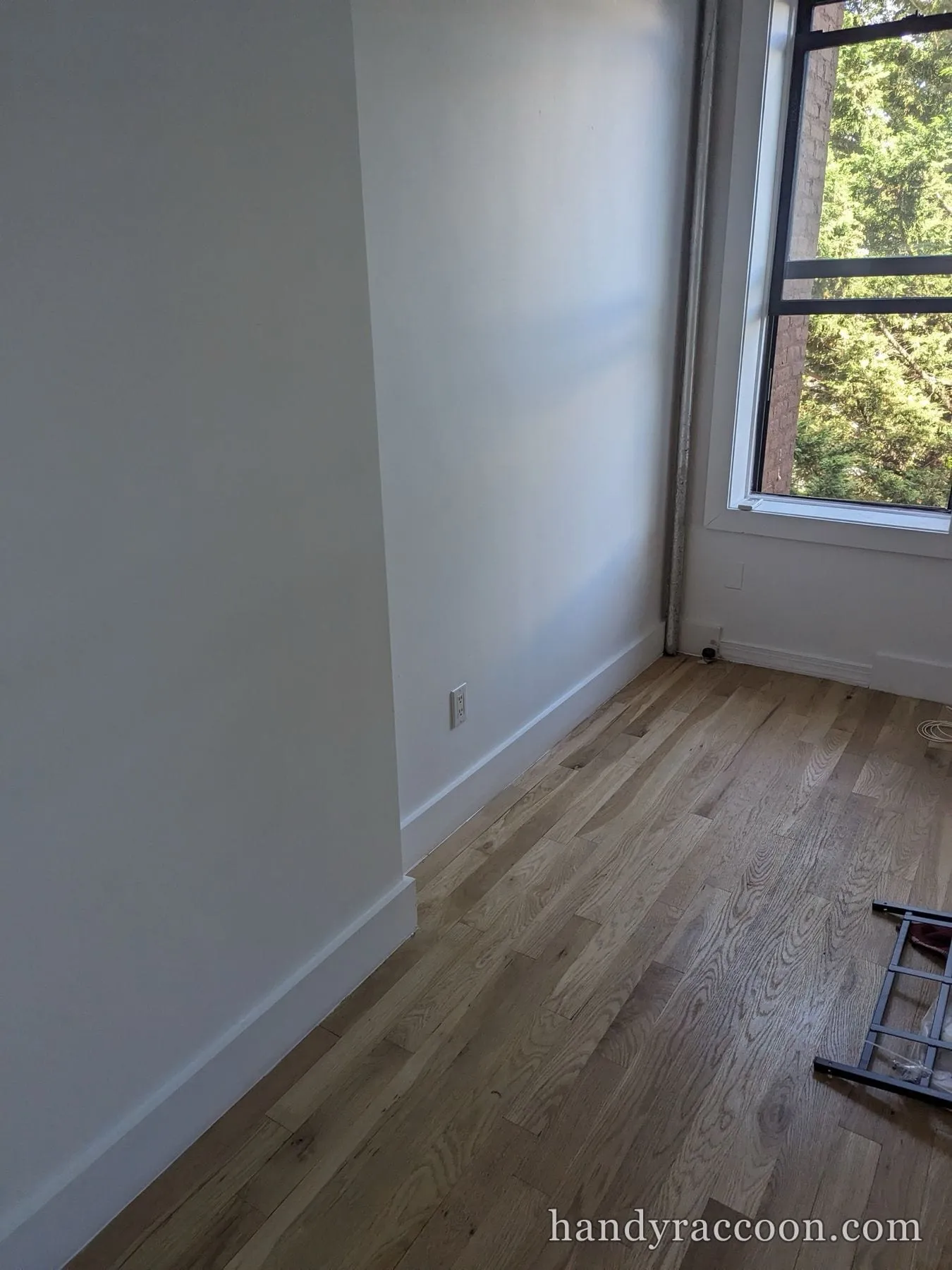 Empty room with white painted walls, white baseboards, hardwood floor and a sunlit window.