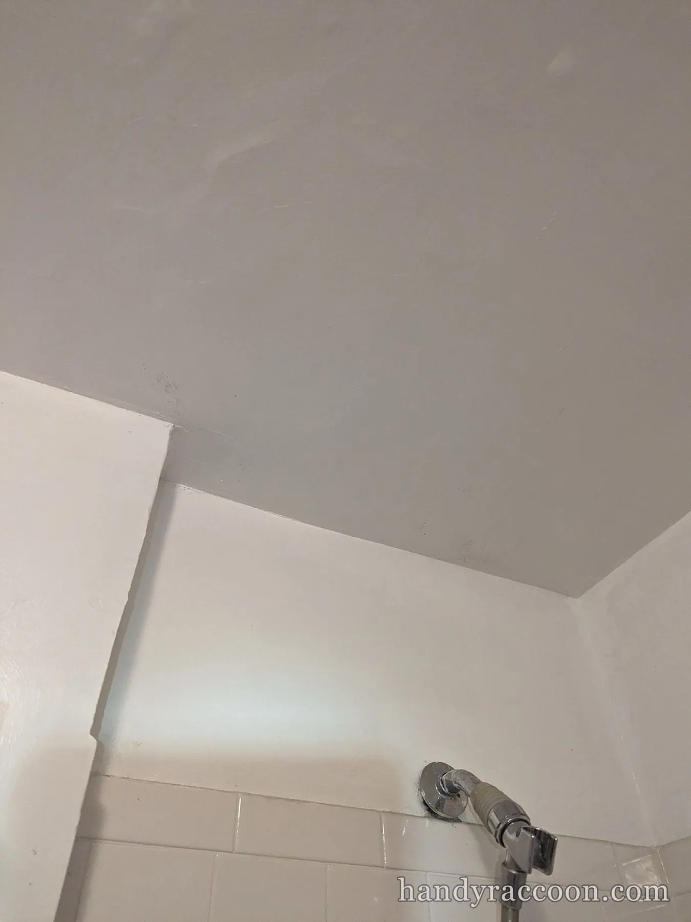 Freshly painted white bathroom ceiling corner above tiled shower wall with a chrome valve.