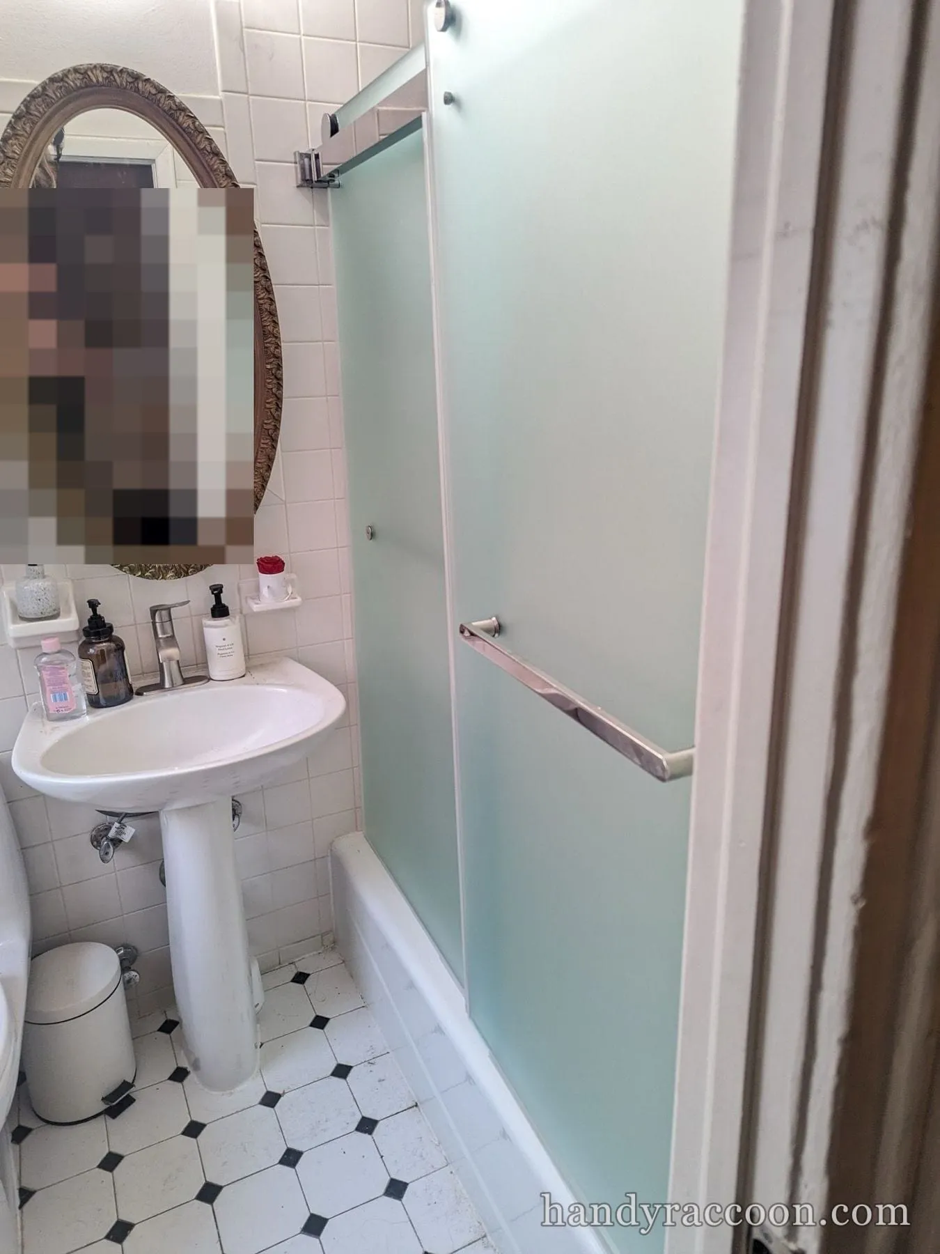 Small tiled bathroom with a frosted sliding glass shower door, pedestal sink, and oval mirror.