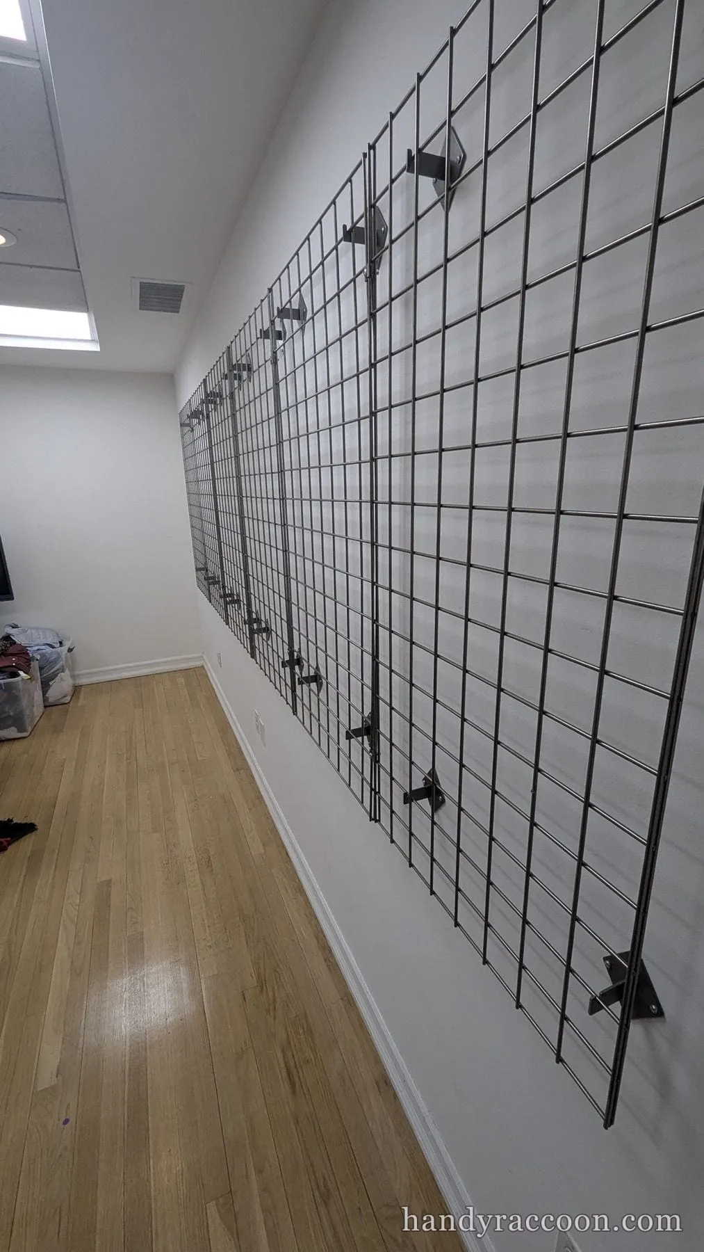 A long wall lined with mounted metal wire grid panels held out on brackets above a wood floor.