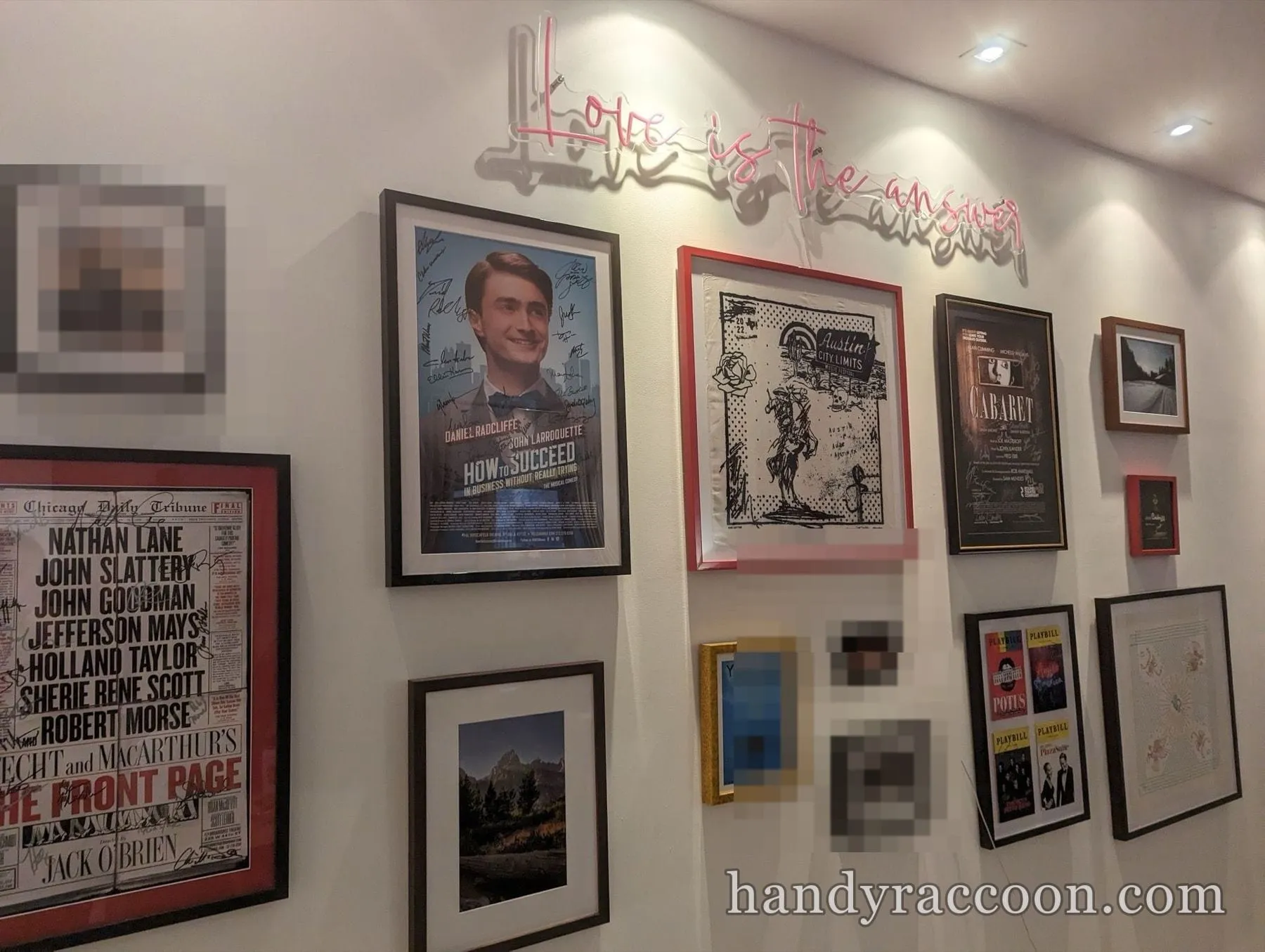 Hallway gallery wall of framed Broadway posters, prints, and a neon sign.
