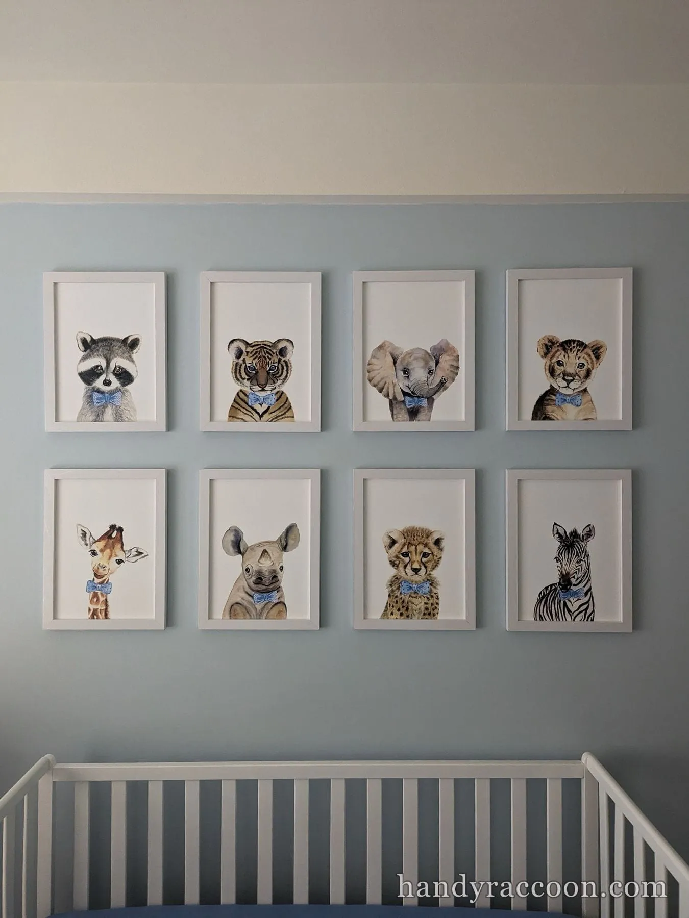 Grid of eight framed baby animal watercolor prints on a blue nursery wall above a crib.