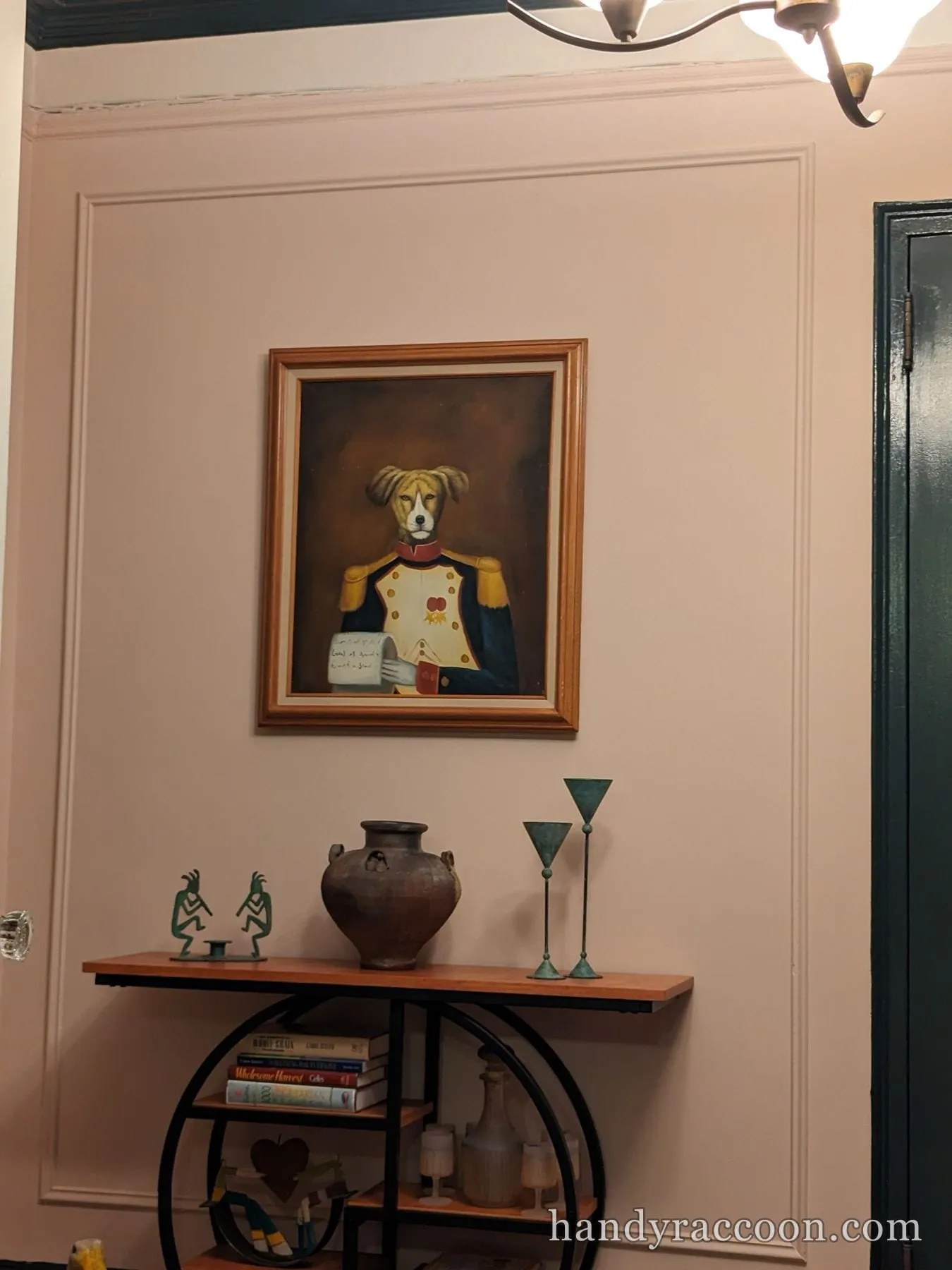 Framed painting of a costumed dog mounted above a wall shelf holding a vase and books.
