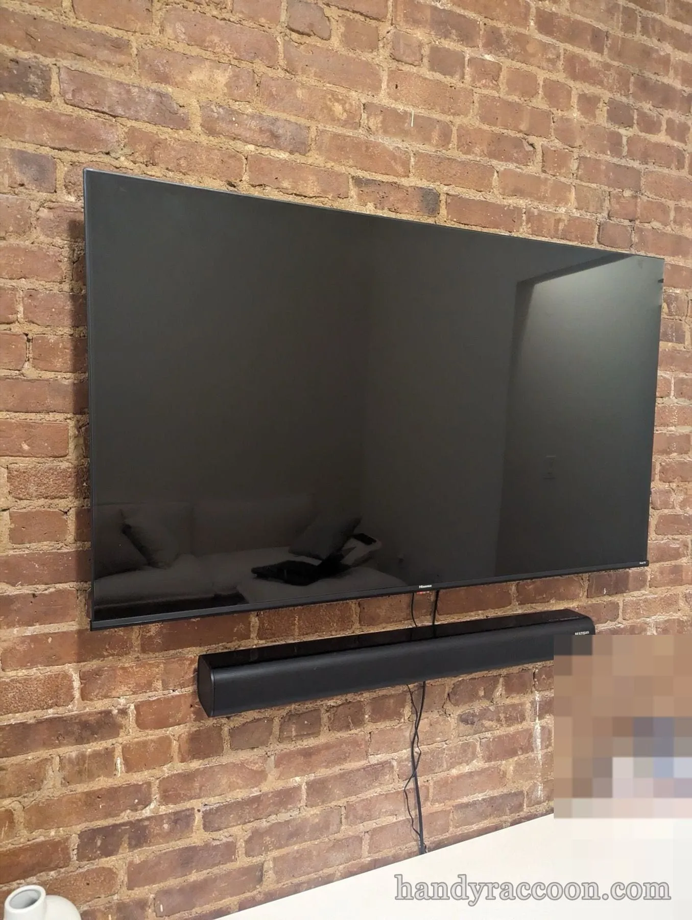 Flat-screen TV mounted on an exposed red brick wall with a black soundbar mounted below.