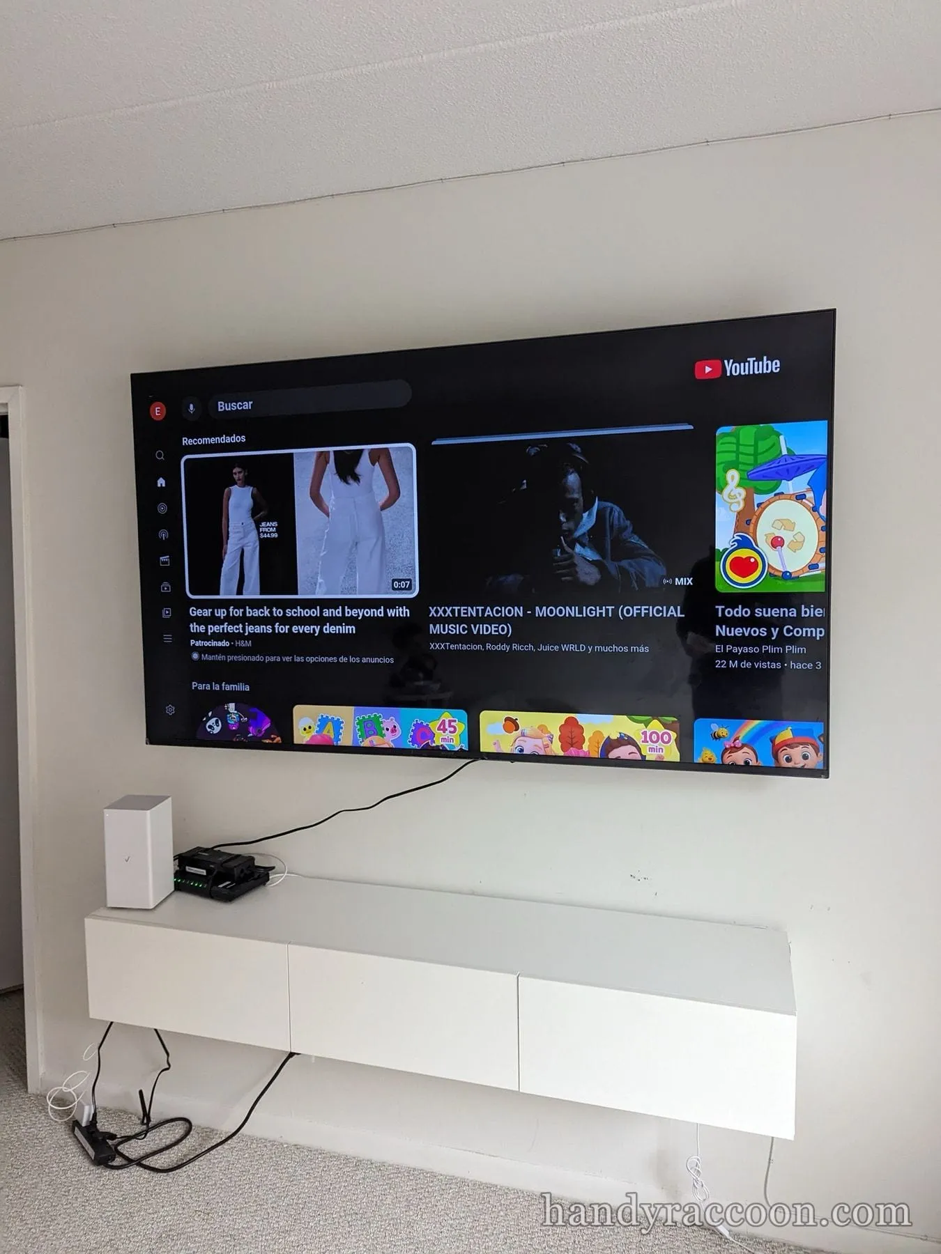 Flat-screen TV mounted above a white floating console displaying a YouTube home screen.