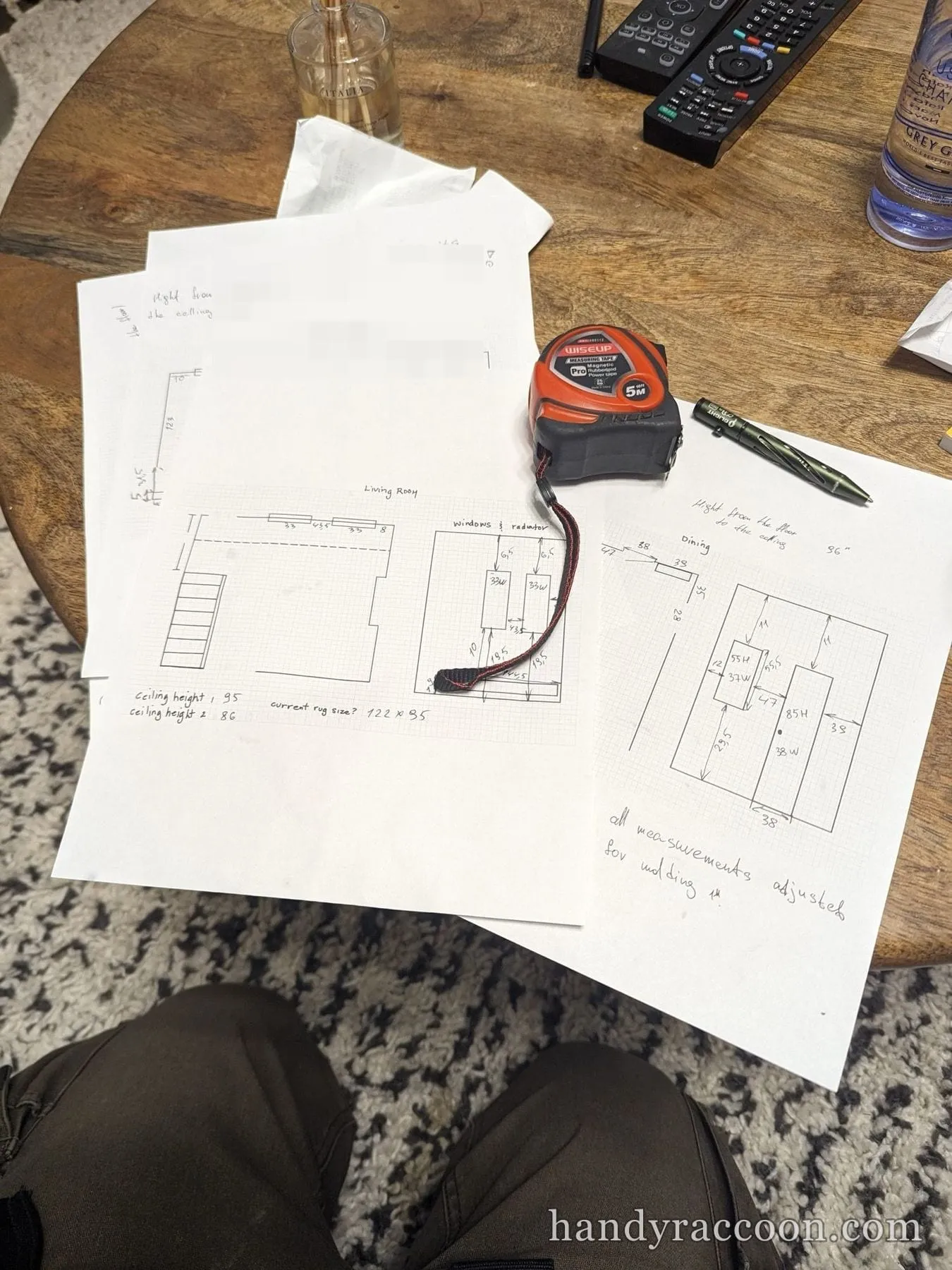 Several handwritten room measurement diagrams on graph paper spread on a table with a tape measure and pen.