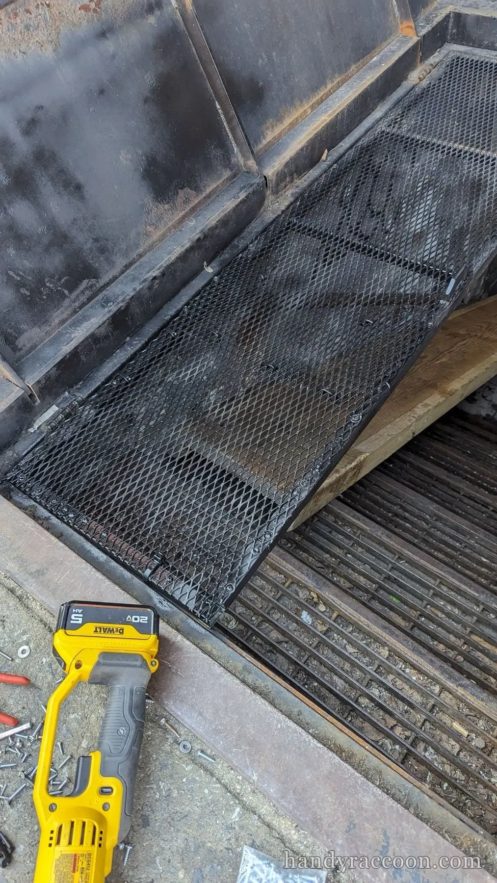 Close-up of black expanded steel mesh stair treads installed on a cellar hatch, with a cordless tool battery on the ground.