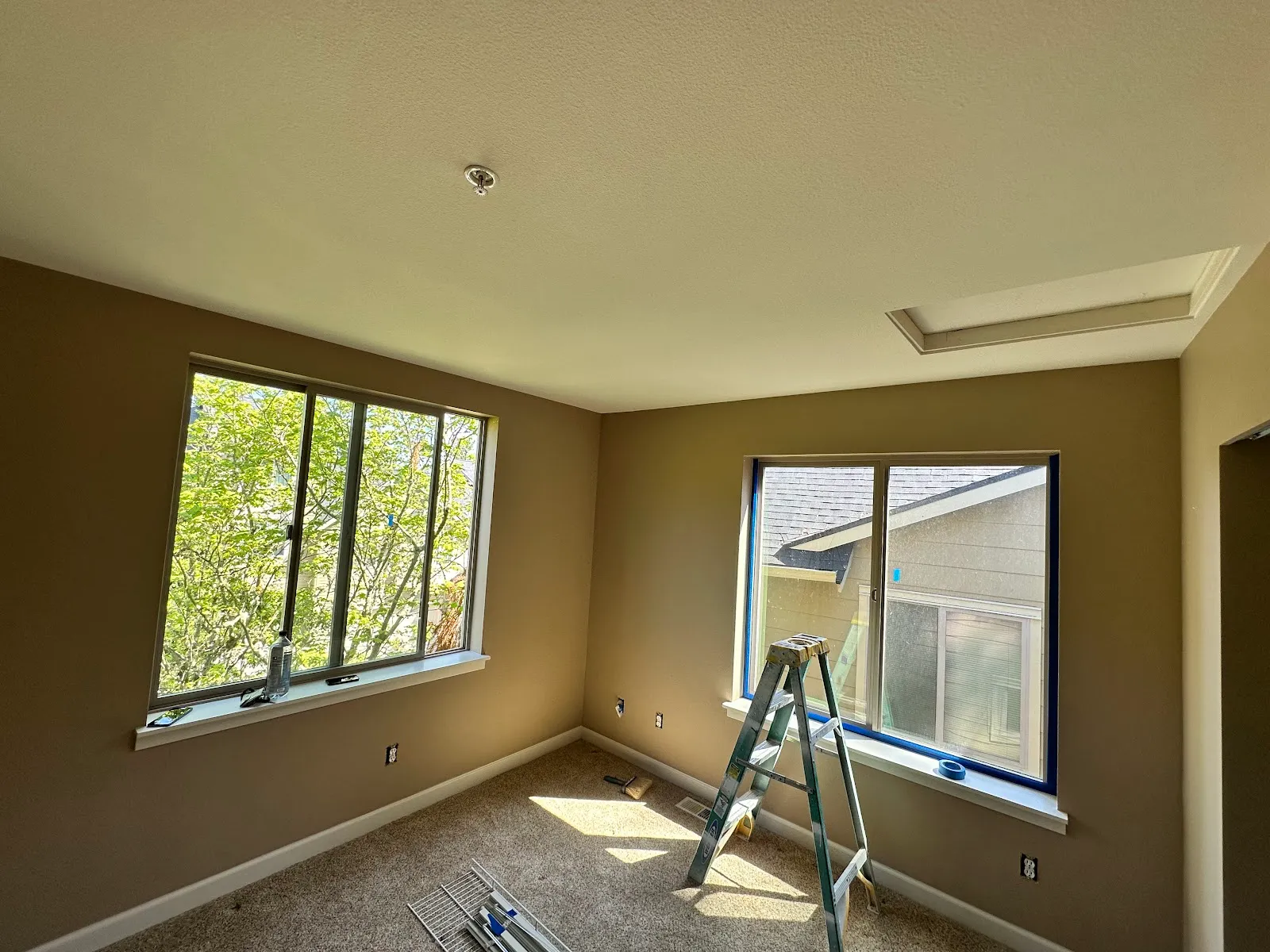 A freshly painted room with taped window trim and a stepladder by the window