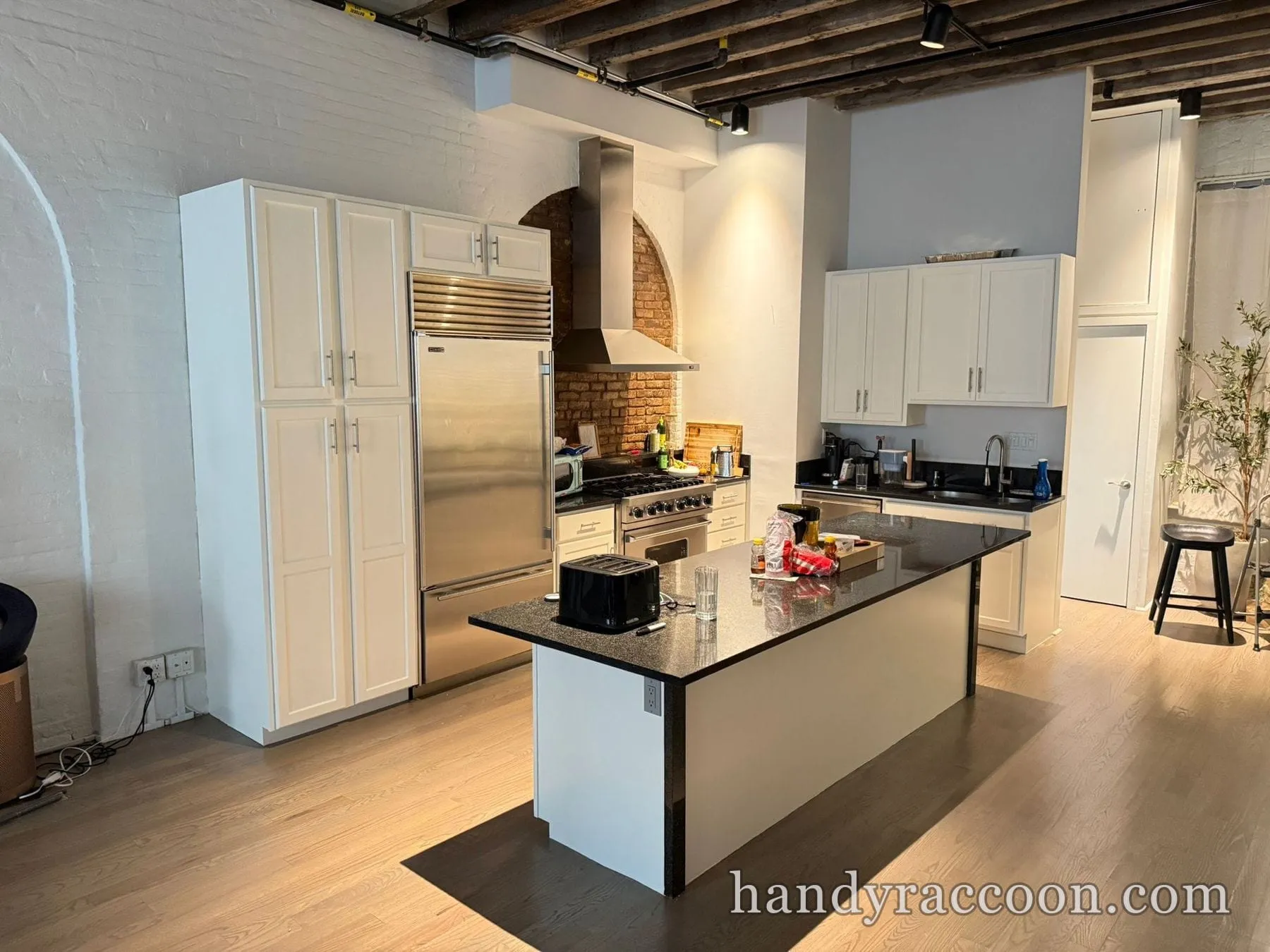 White painted kitchen cabinets with stainless fridge, black island and brick backsplash in a loft.