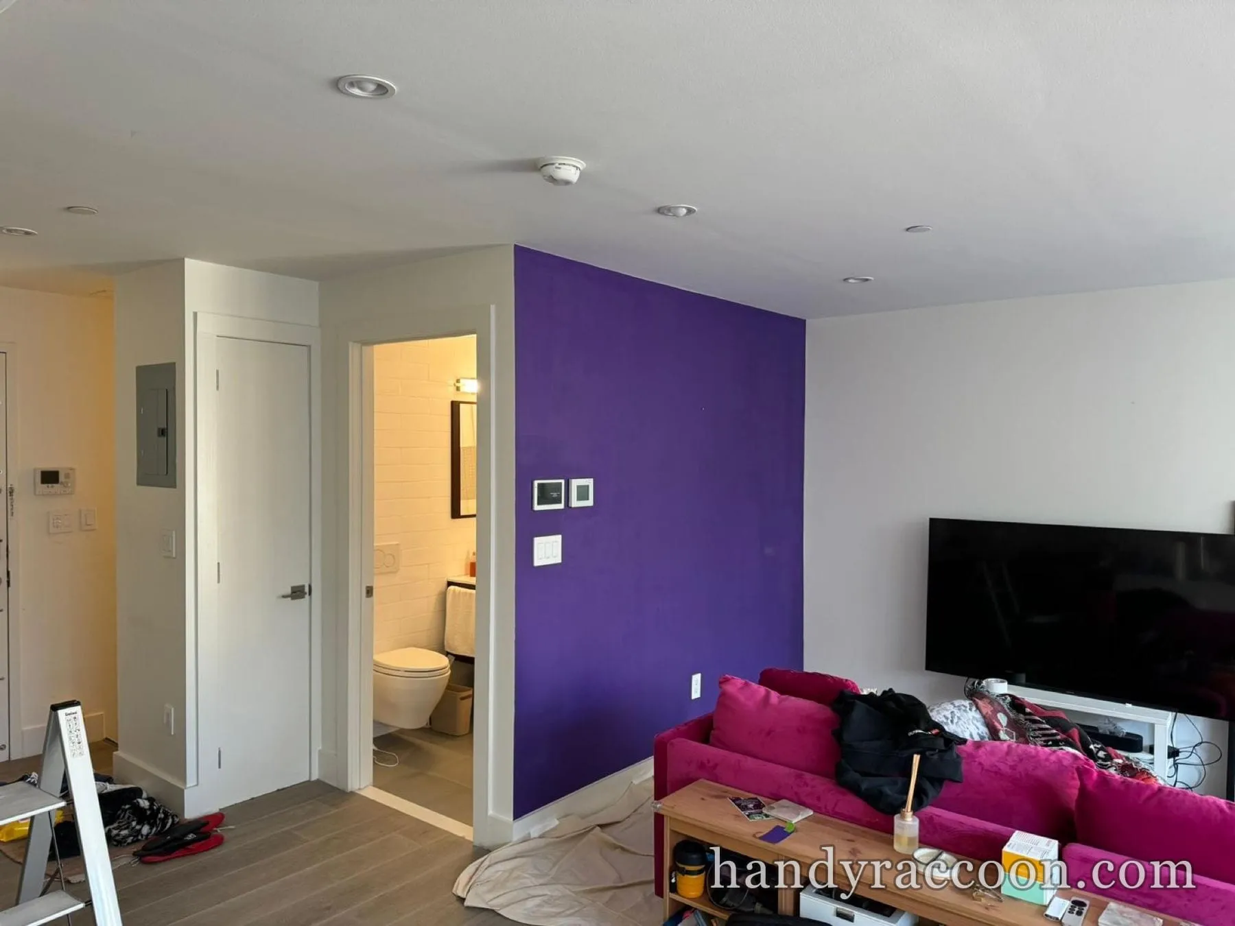 Living room with a freshly painted deep purple accent wall next to a bathroom doorway.