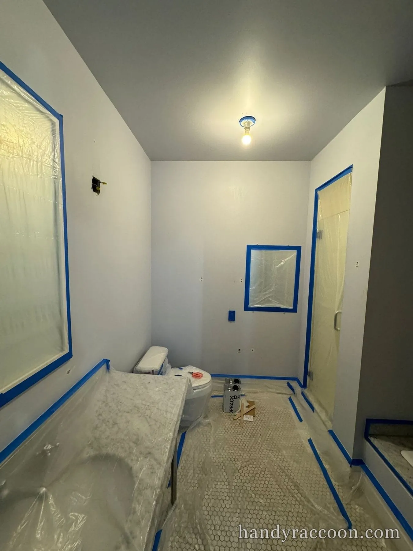 Bathroom with walls taped and floor and fixtures covered in plastic sheeting before painting.