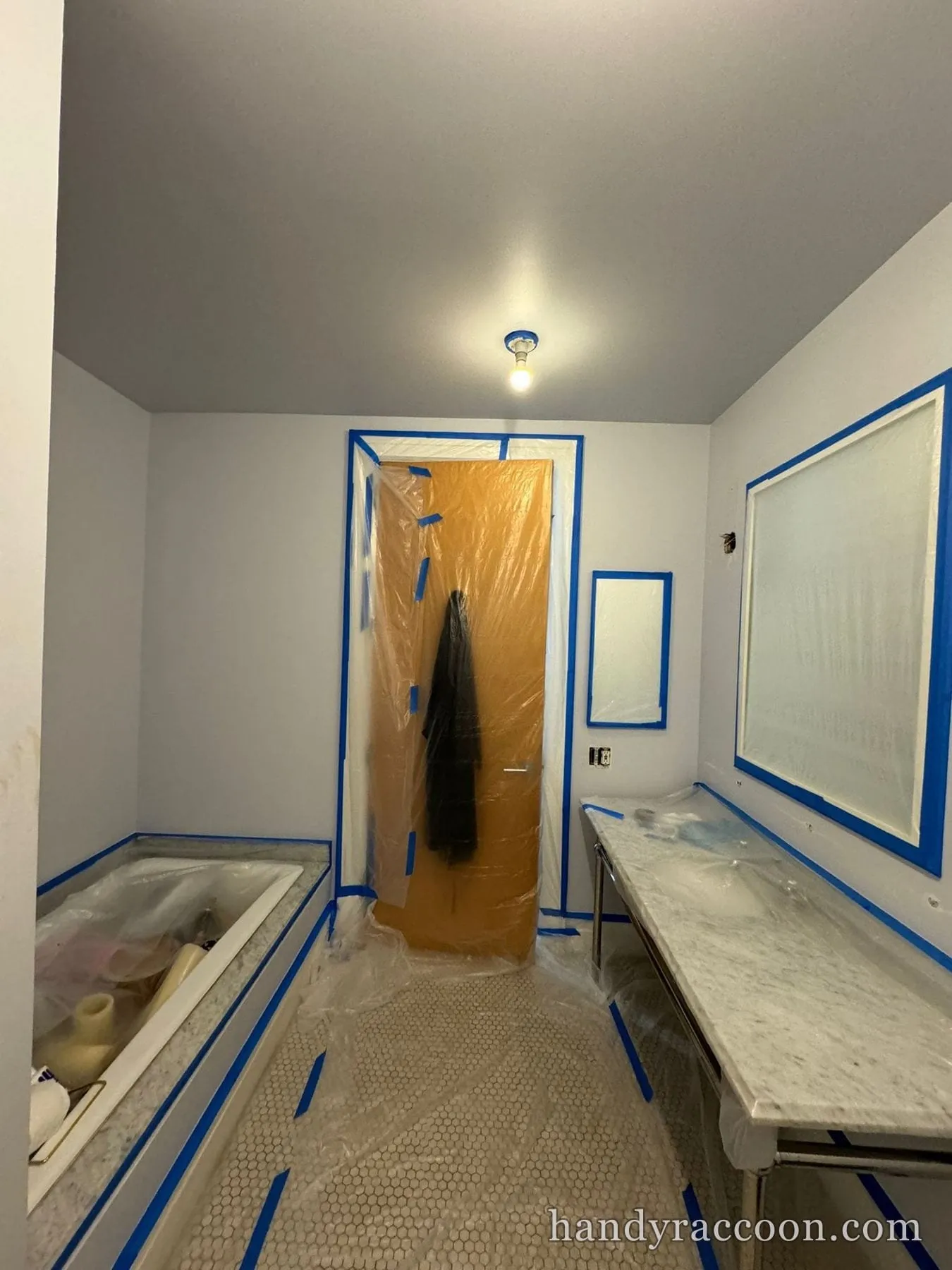 Bathroom with bathtub, marble vanity, and door covered in protective plastic and blue tape.