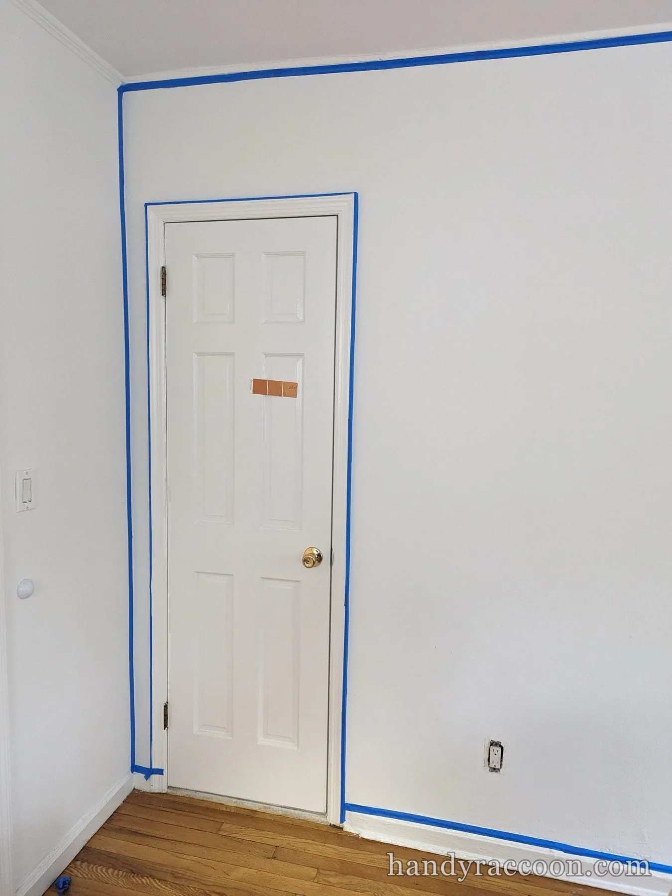 White paneled door and surrounding wall edges masked with blue tape before painting.