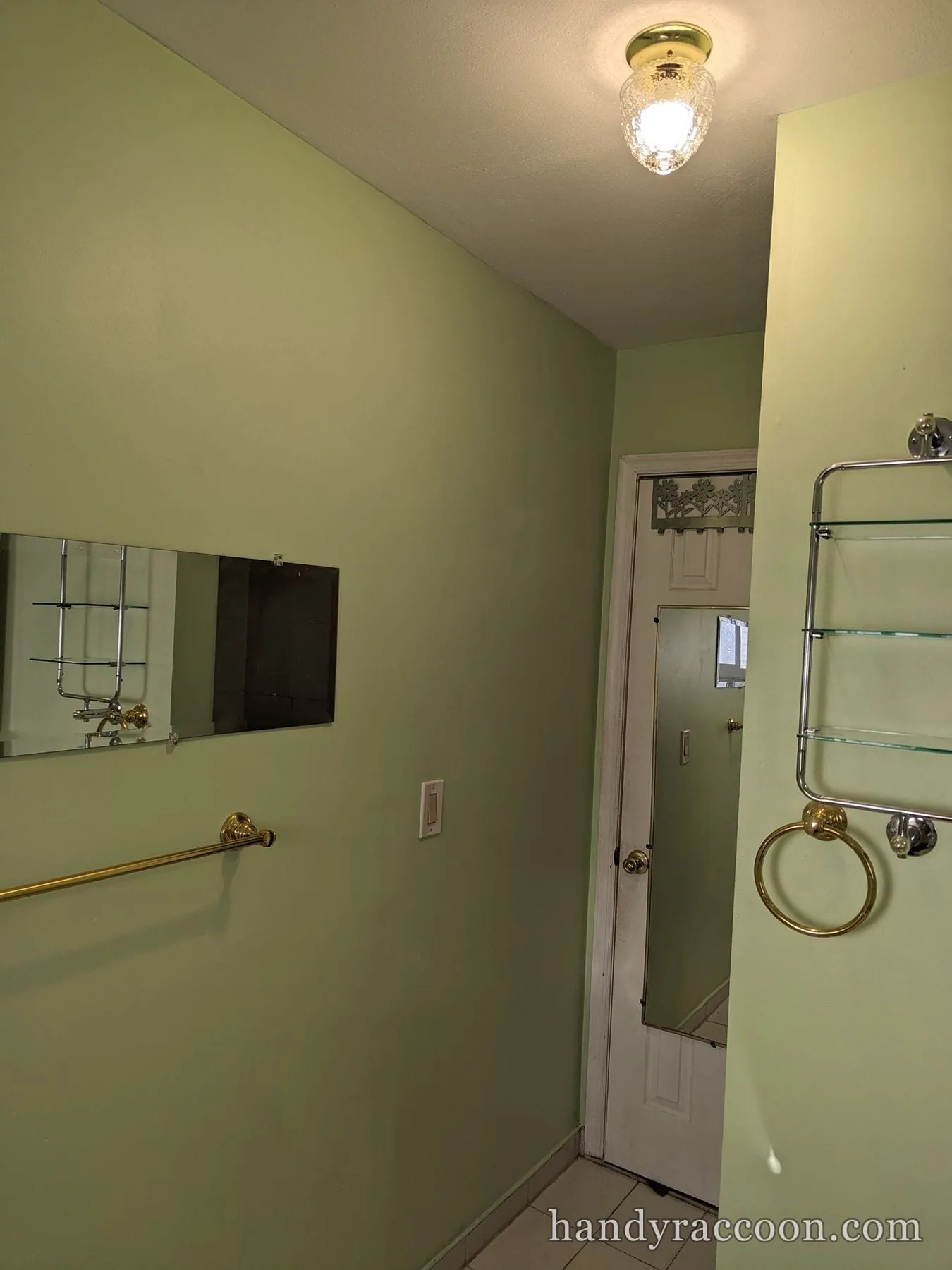 Bathroom painted light green with brass towel bar, towel ring and glass shelving.