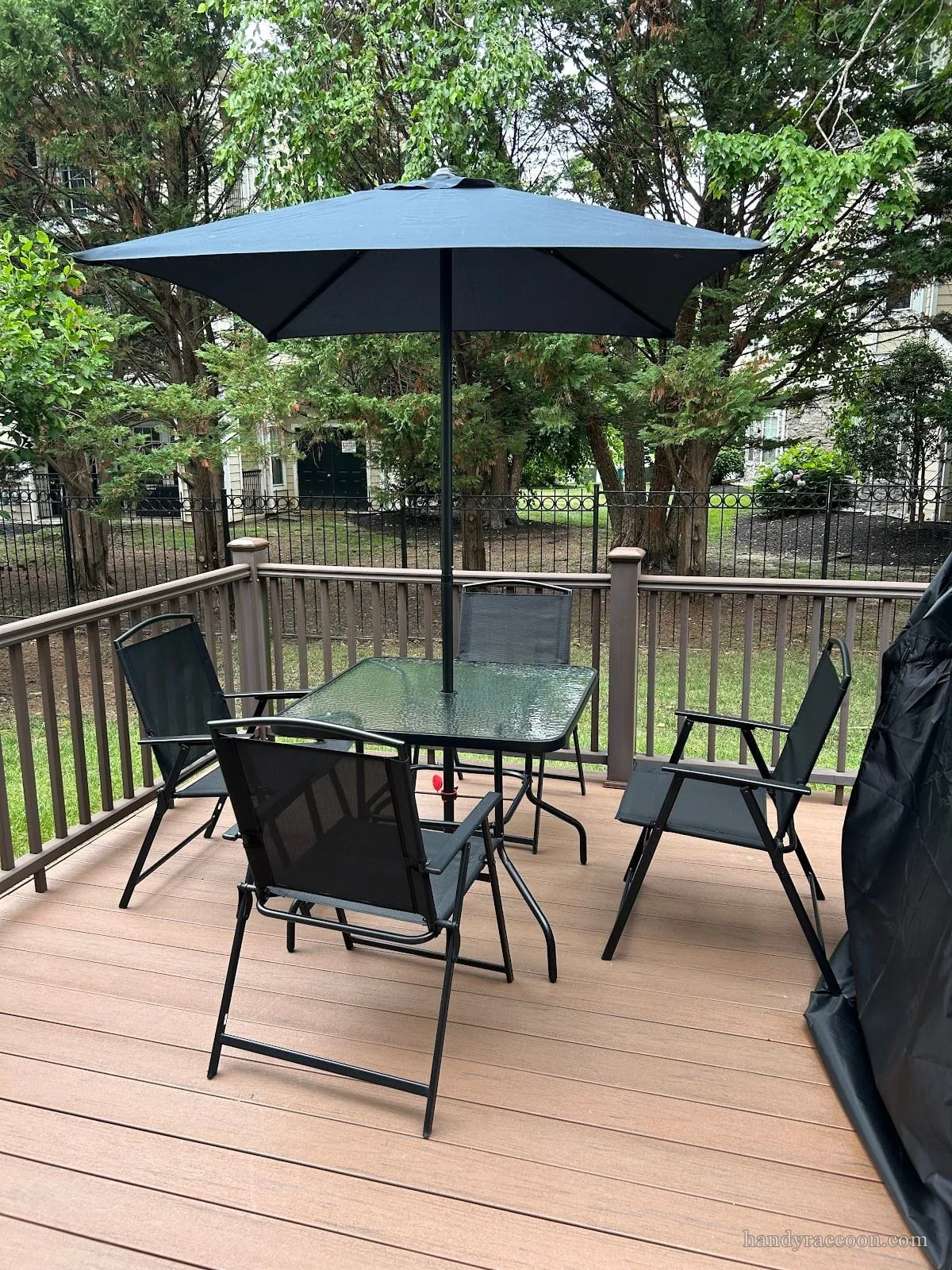 An assembled patio set on a deck: glass table, four folding chairs and an umbrella