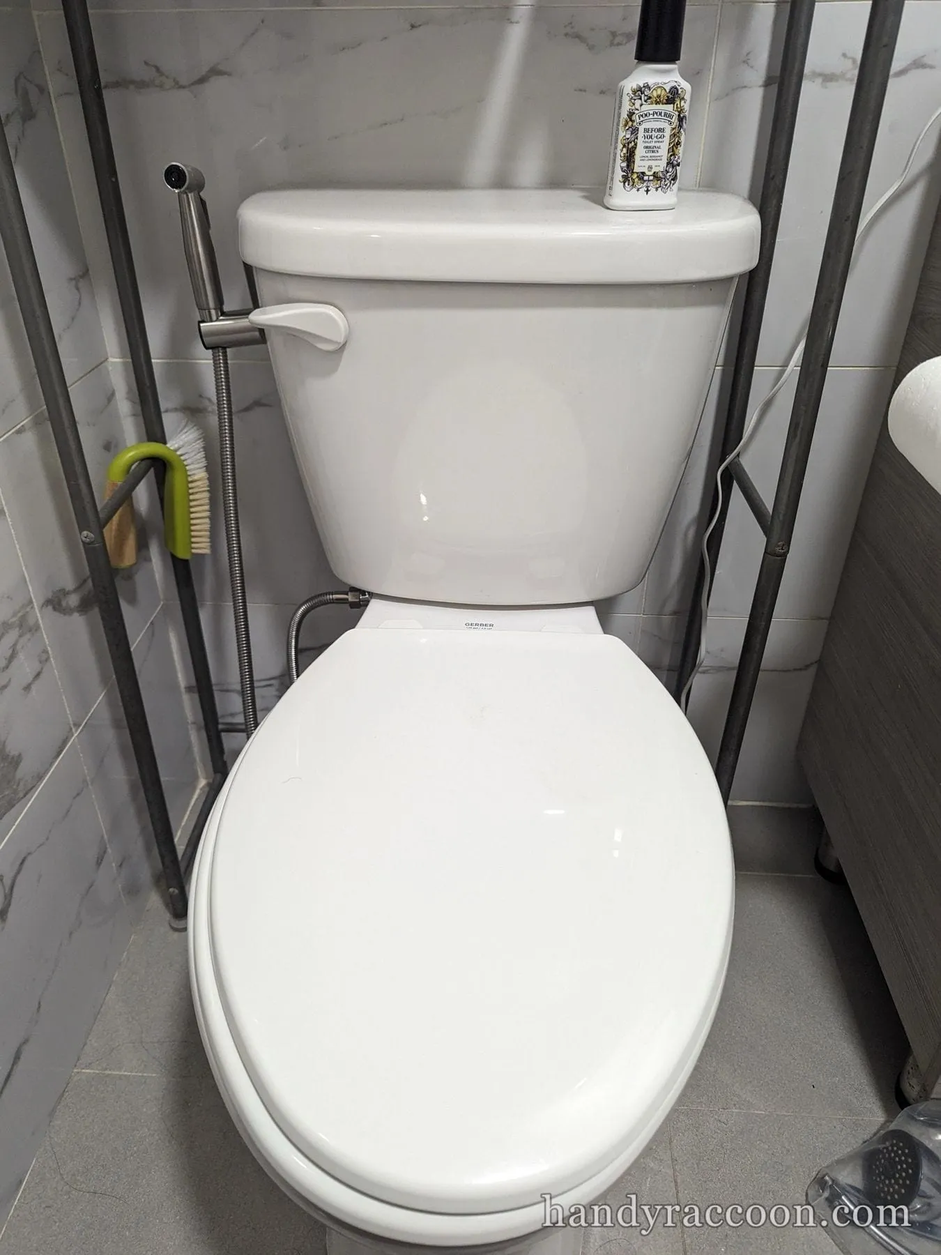 White two-piece toilet with a handheld bidet sprayer attached, on a gray marble tile wall.