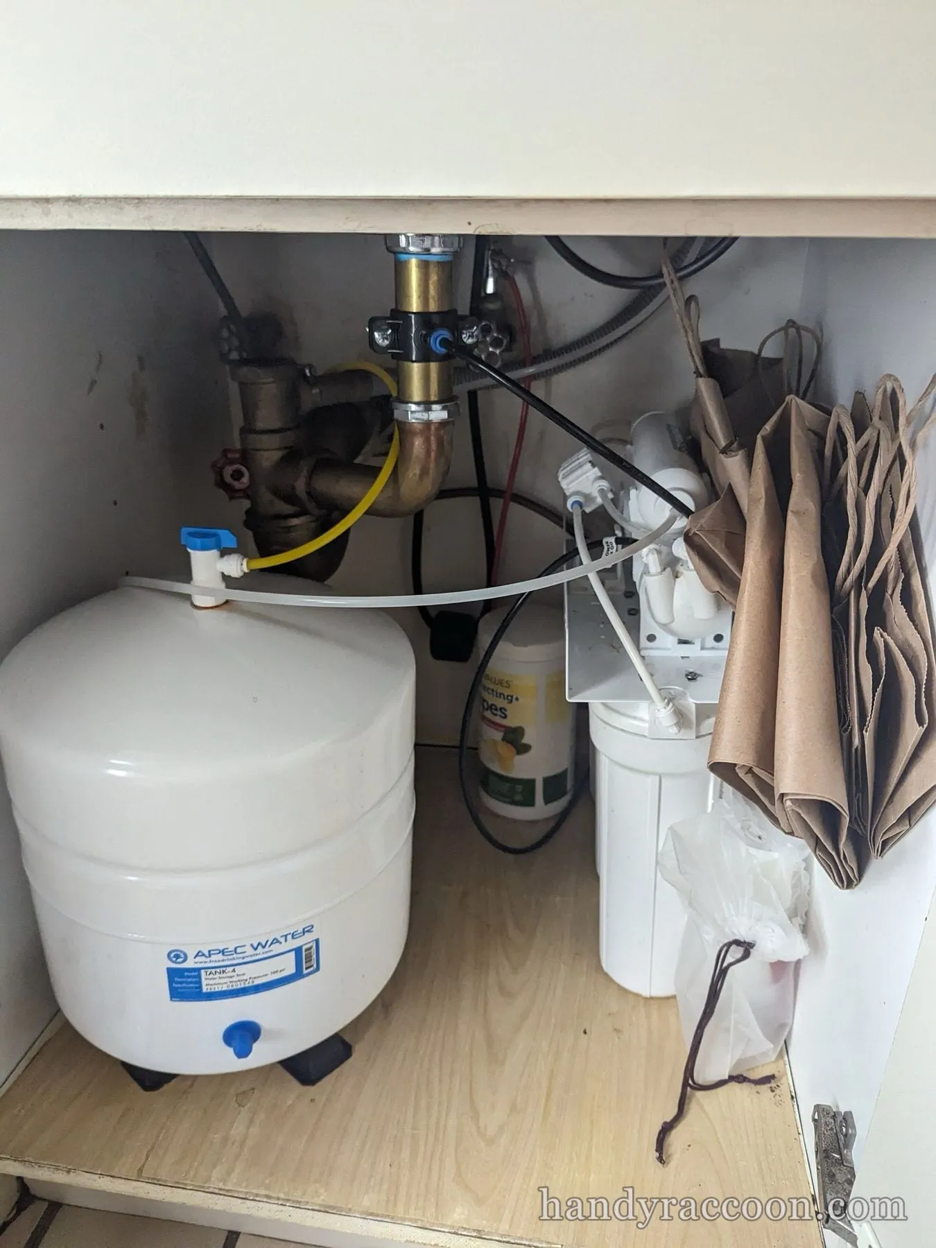 Installed under-sink reverse osmosis filter system with white storage tank and filter housings.